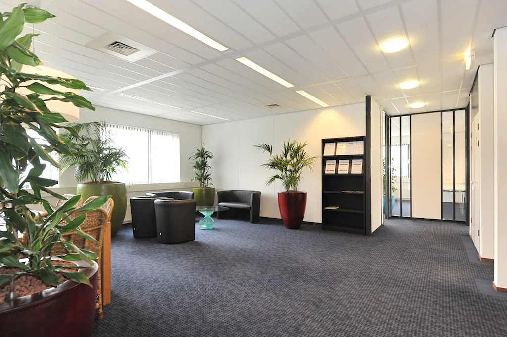 Moderne wachtruimte in een kantoorpand aan de Laan van ‘s-Gravenmade met planten, zitgelegenheid en een open boekenkast.